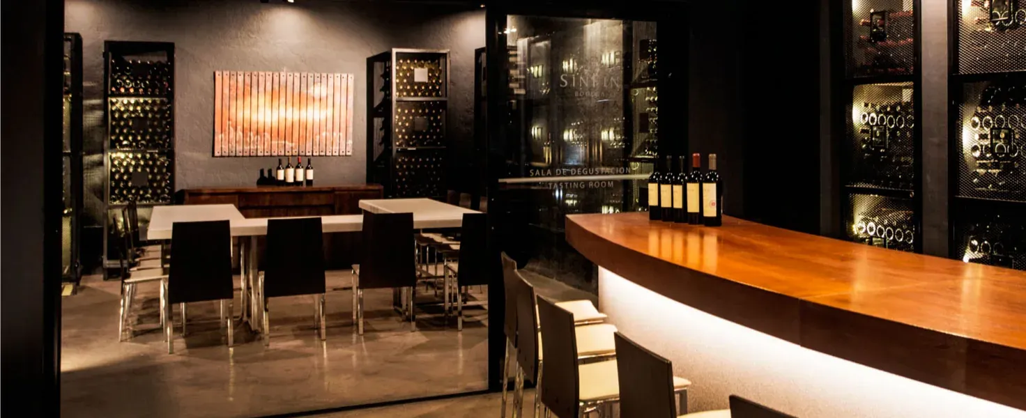 Sala de degustación de la bodega, con barra curva de madera y botelleros iluminados