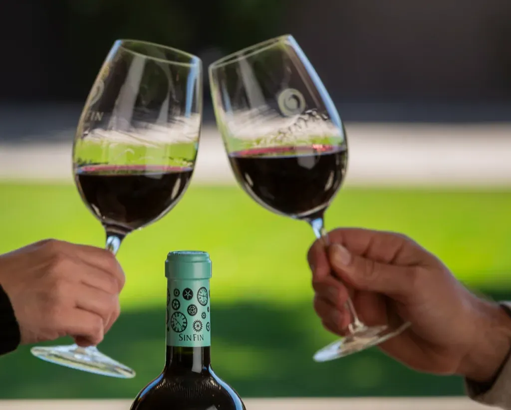 Dos personas brindan con copas grabadas SinFin junto a una botella de la bodega