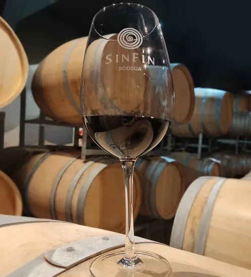 Copa grabada con el logo SinFin y vino tinto, apoyada sobre una barrica