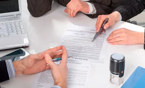 Reunión de trabajo alrededor de una mesa, con documentos, lapiceras y una computadora portátil